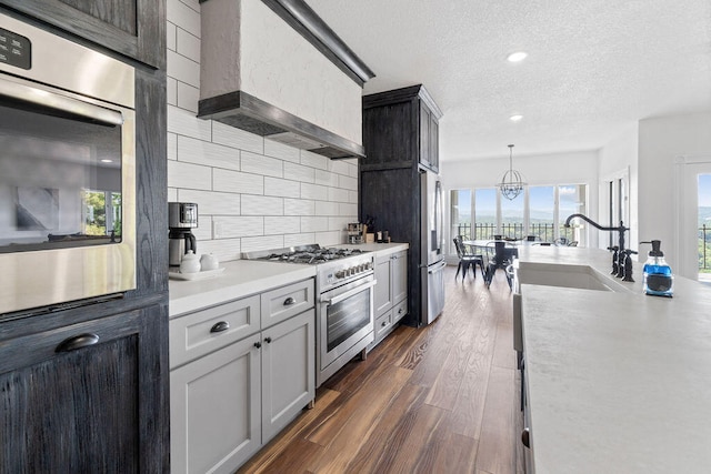 kitchen with decorative backsplash, wall chimney range hood, stainless steel appliances, sink, and decorative light fixtures