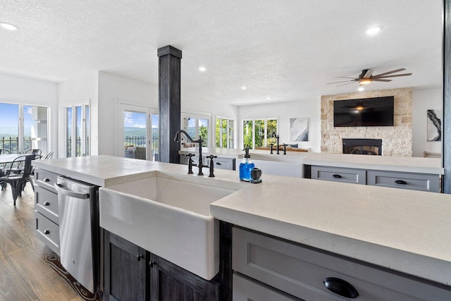 kitchen with wood-type flooring, sink, a stone fireplace, a textured ceiling, and ceiling fan