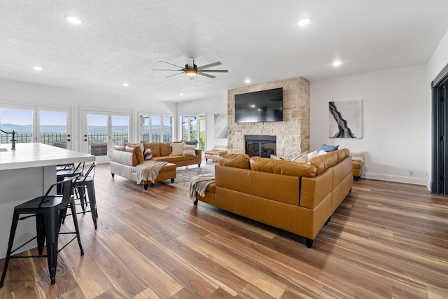 living room featuring dark wood-type flooring, ceiling fan, a stone fireplace, and a textured ceiling