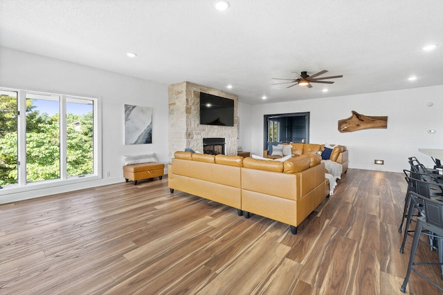 living room with ceiling fan, a stone fireplace, and hardwood / wood-style floors