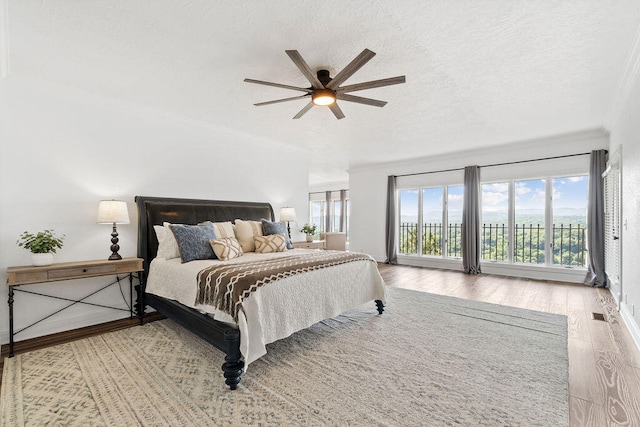 bedroom featuring ceiling fan, a textured ceiling, access to exterior, light hardwood / wood-style flooring, and crown molding