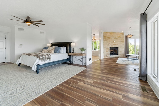 bedroom featuring a large fireplace, ensuite bath, dark hardwood / wood-style flooring, and ceiling fan