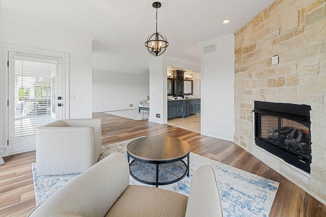 living room with a notable chandelier, ornamental molding, hardwood / wood-style flooring, and a fireplace