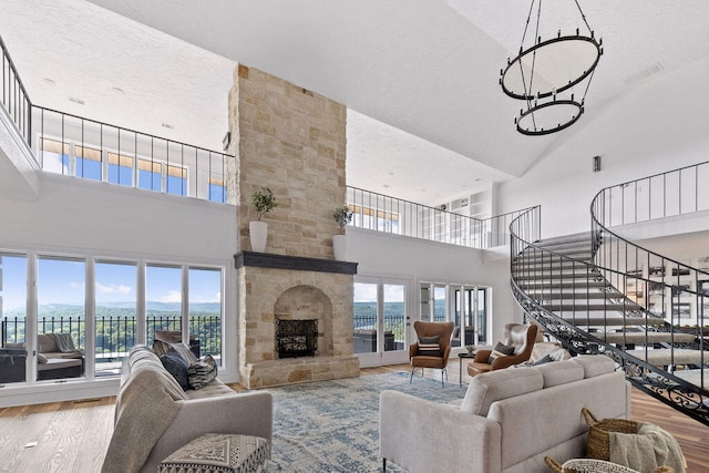 living room featuring a healthy amount of sunlight, high vaulted ceiling, a stone fireplace, and hardwood / wood-style floors