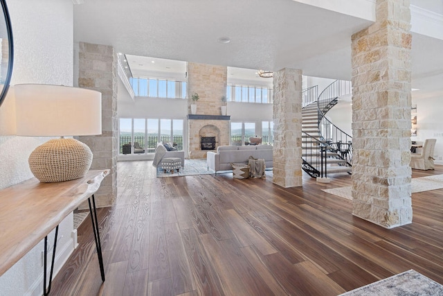 entryway featuring a towering ceiling, ornate columns, a stone fireplace, and wood-type flooring