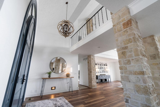 entryway with a notable chandelier, dark wood-type flooring, ornate columns, and a towering ceiling