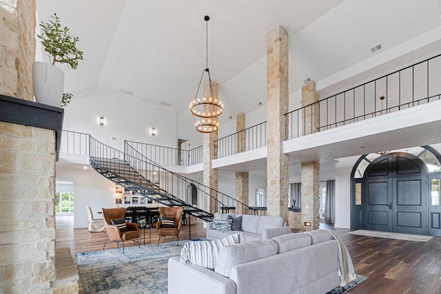 living room featuring dark wood-type flooring, high vaulted ceiling, decorative columns, and a chandelier