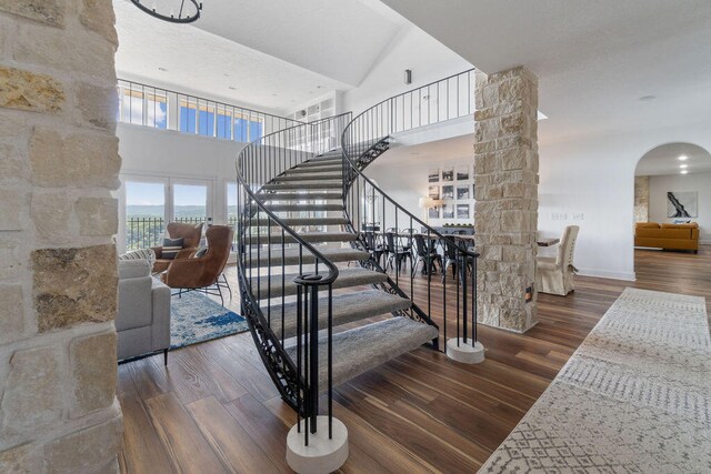 stairs with hardwood / wood-style floors, high vaulted ceiling, and decorative columns