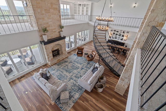 living room with a towering ceiling, a notable chandelier, hardwood / wood-style flooring, and a stone fireplace