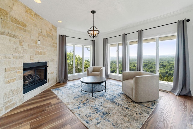 living room with wood-type flooring, a stone fireplace, a textured ceiling, crown molding, and a chandelier