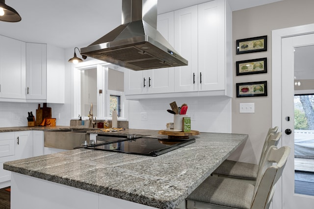 kitchen featuring stone countertops, island exhaust hood, white cabinetry, and tasteful backsplash