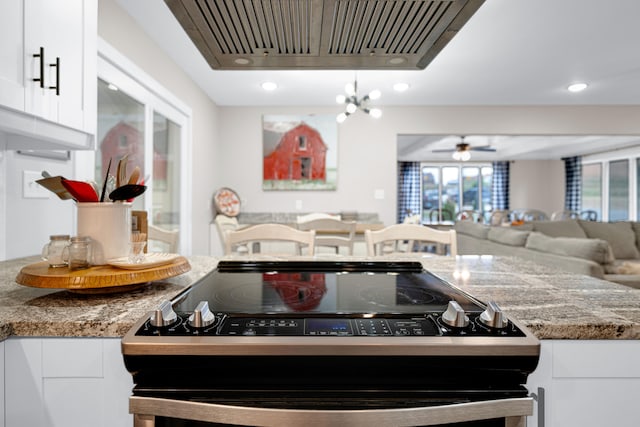 kitchen featuring ceiling fan with notable chandelier, white cabinetry, stainless steel stove, range hood, and light stone counters