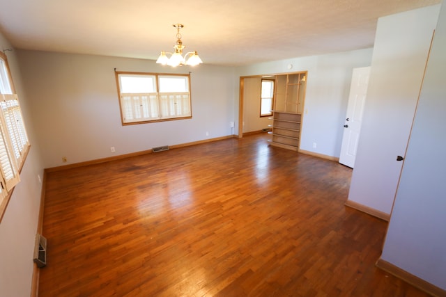 unfurnished room with an inviting chandelier and dark hardwood / wood-style flooring