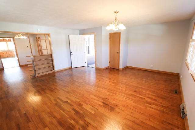 empty room featuring an inviting chandelier, a healthy amount of sunlight, and hardwood / wood-style flooring