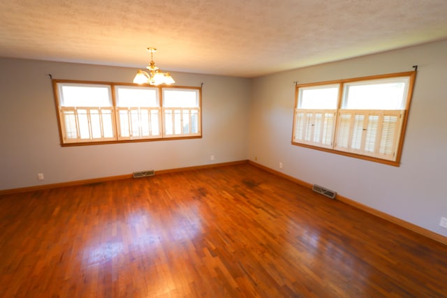 empty room featuring a textured ceiling, dark hardwood / wood-style floors, an inviting chandelier, and plenty of natural light