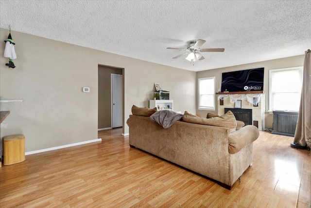 living room with ceiling fan, wood-type flooring, a textured ceiling, and a fireplace