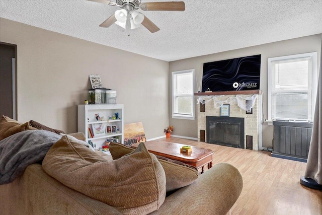 living room featuring a brick fireplace, wood-type flooring, a textured ceiling, and ceiling fan