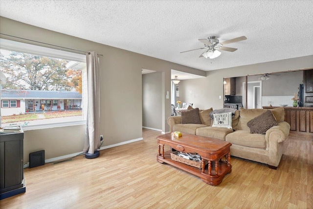 living room with ceiling fan, a textured ceiling, and light hardwood / wood-style flooring