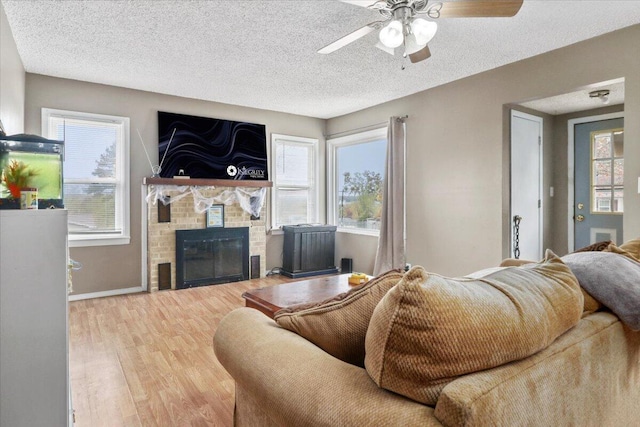 living room featuring a textured ceiling, wood-type flooring, ceiling fan, and a fireplace