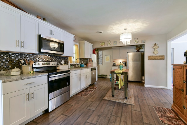 kitchen featuring light stone counters, stainless steel appliances, white cabinetry, pendant lighting, and dark wood-type flooring