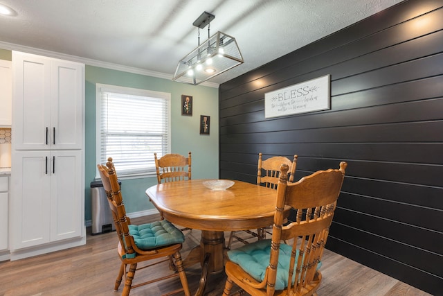 dining room with ornamental molding, light hardwood / wood-style floors, wood walls, and a textured ceiling