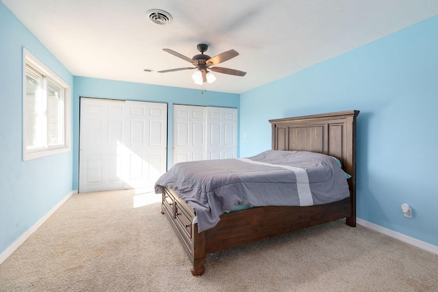 bedroom with multiple closets, light carpet, and ceiling fan