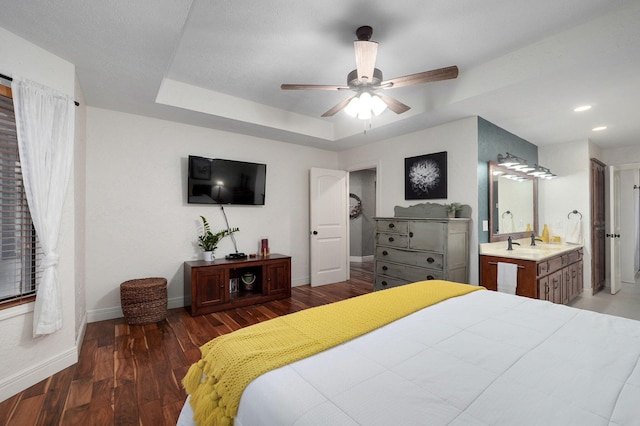 bedroom featuring connected bathroom, dark hardwood / wood-style flooring, a tray ceiling, and ceiling fan