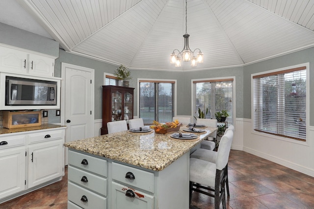 kitchen with white cabinets, a kitchen island, stainless steel microwave, and decorative light fixtures