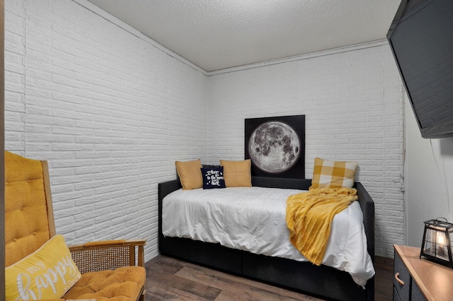 bedroom with dark hardwood / wood-style flooring, brick wall, and a textured ceiling