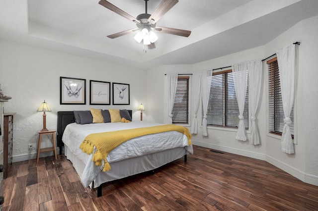 bedroom with ceiling fan, a raised ceiling, and dark hardwood / wood-style flooring