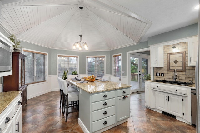 kitchen featuring a kitchen island, decorative light fixtures, light stone countertops, sink, and white cabinets