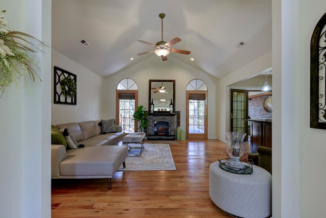 living room with a stone fireplace, ceiling fan, vaulted ceiling, and light hardwood / wood-style floors