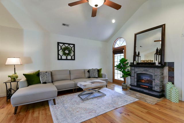 living room featuring ceiling fan, light hardwood / wood-style floors, a stone fireplace, and vaulted ceiling