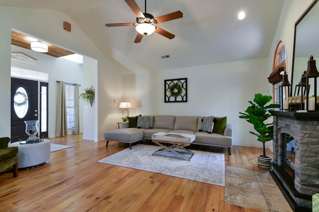 living room with ceiling fan, a stone fireplace, light hardwood / wood-style flooring, and lofted ceiling