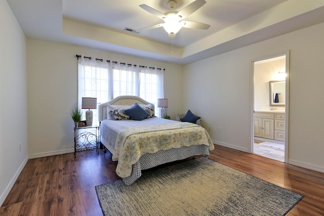 bedroom featuring dark hardwood / wood-style floors, ceiling fan, a tray ceiling, and connected bathroom