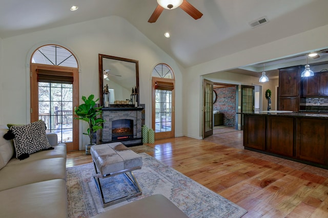 living room with high vaulted ceiling, ceiling fan, light hardwood / wood-style floors, and a fireplace