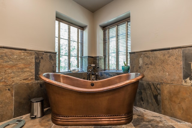 interior space with a wealth of natural light, a tub to relax in, and tile walls