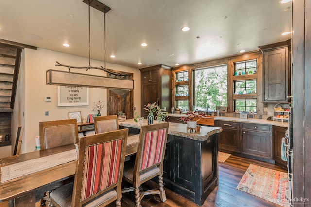 kitchen featuring dark hardwood / wood-style flooring, light stone counters, decorative backsplash, hanging light fixtures, and a kitchen island