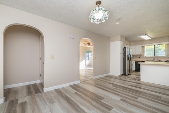 kitchen featuring stainless steel fridge with ice dispenser, a textured ceiling, hanging light fixtures, white cabinets, and light hardwood / wood-style flooring