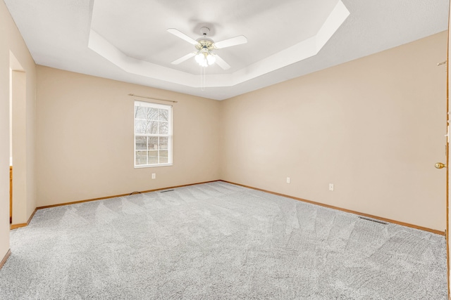 carpeted empty room with ceiling fan and a tray ceiling