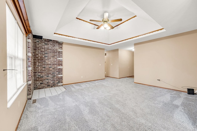 carpeted spare room featuring ceiling fan, brick wall, and a raised ceiling