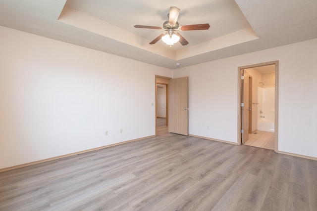 unfurnished bedroom featuring light wood-type flooring, ceiling fan, a tray ceiling, and connected bathroom