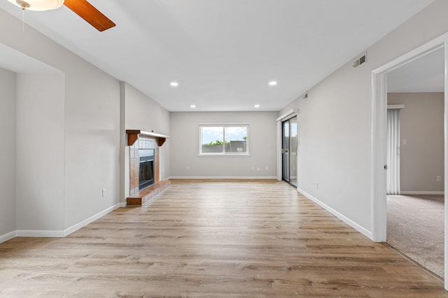 unfurnished living room with a tiled fireplace, light hardwood / wood-style flooring, and ceiling fan