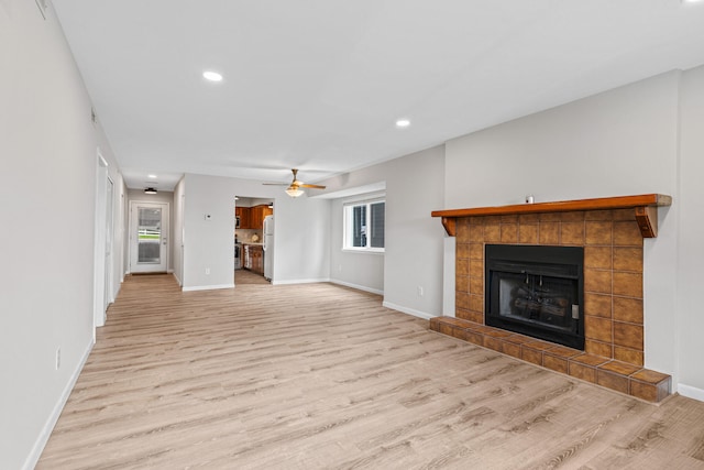 unfurnished living room with a tiled fireplace, light hardwood / wood-style flooring, and ceiling fan