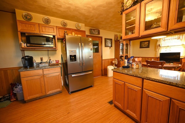 kitchen featuring stainless steel appliances, wooden walls, a textured ceiling, light hardwood / wood-style flooring, and dark stone countertops