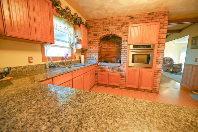 kitchen featuring sink, light hardwood / wood-style floors, dark stone countertops, oven, and brick wall