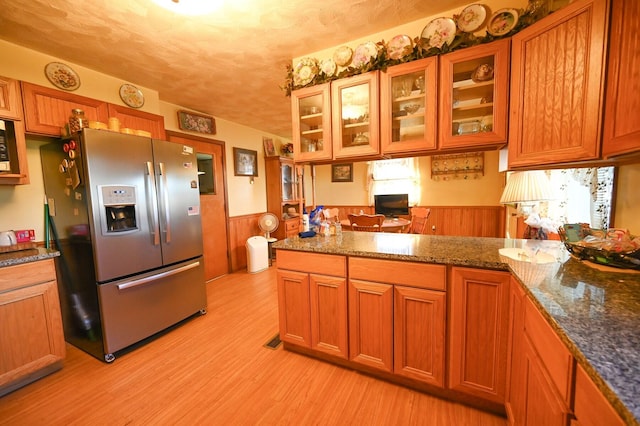 kitchen featuring dark stone counters, appliances with stainless steel finishes, a textured ceiling, wood walls, and light hardwood / wood-style flooring