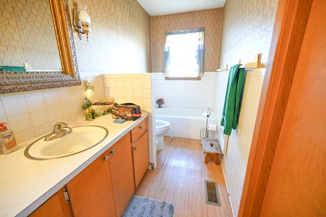 bathroom featuring a bathtub, tile walls, vanity, hardwood / wood-style flooring, and toilet