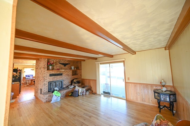 living room featuring wood walls, beamed ceiling, wood-type flooring, and a brick fireplace