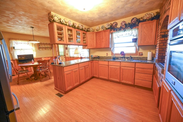 kitchen featuring sink, appliances with stainless steel finishes, kitchen peninsula, hanging light fixtures, and light wood-type flooring